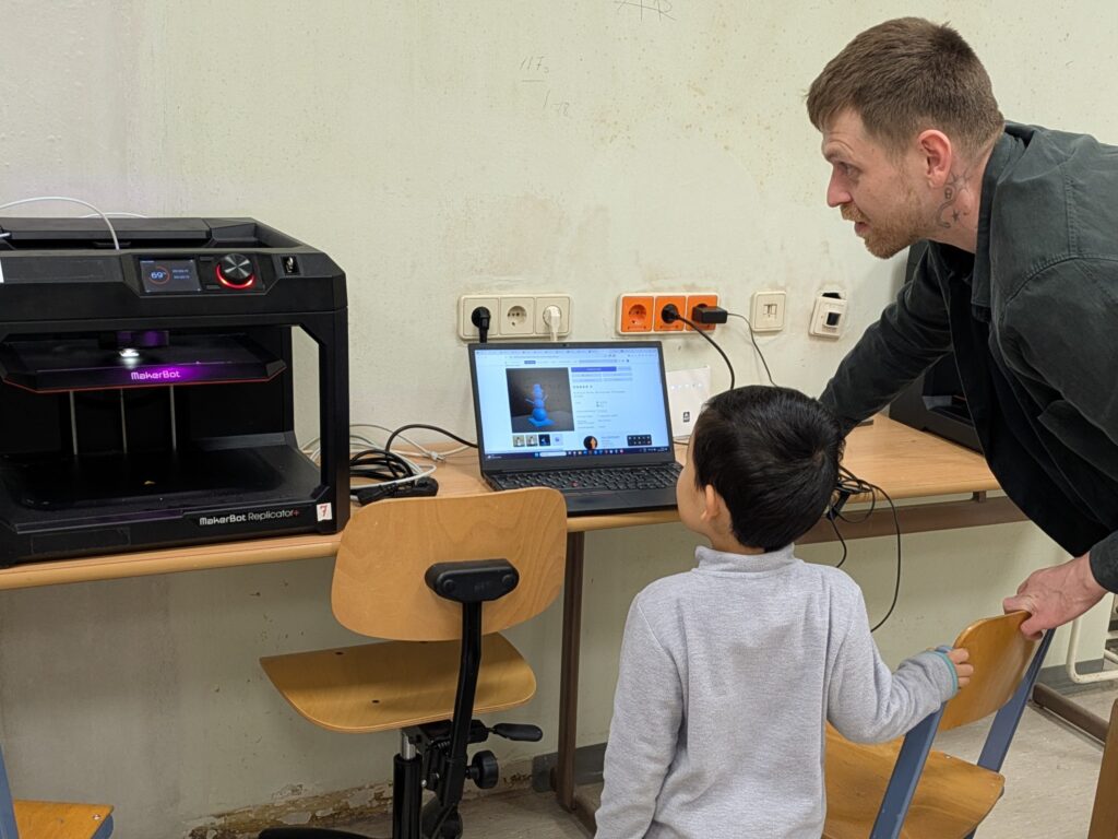 Kind und TU Studierender und Transformer Mitarbeiter beim 3D-Druck eines Schneemanns