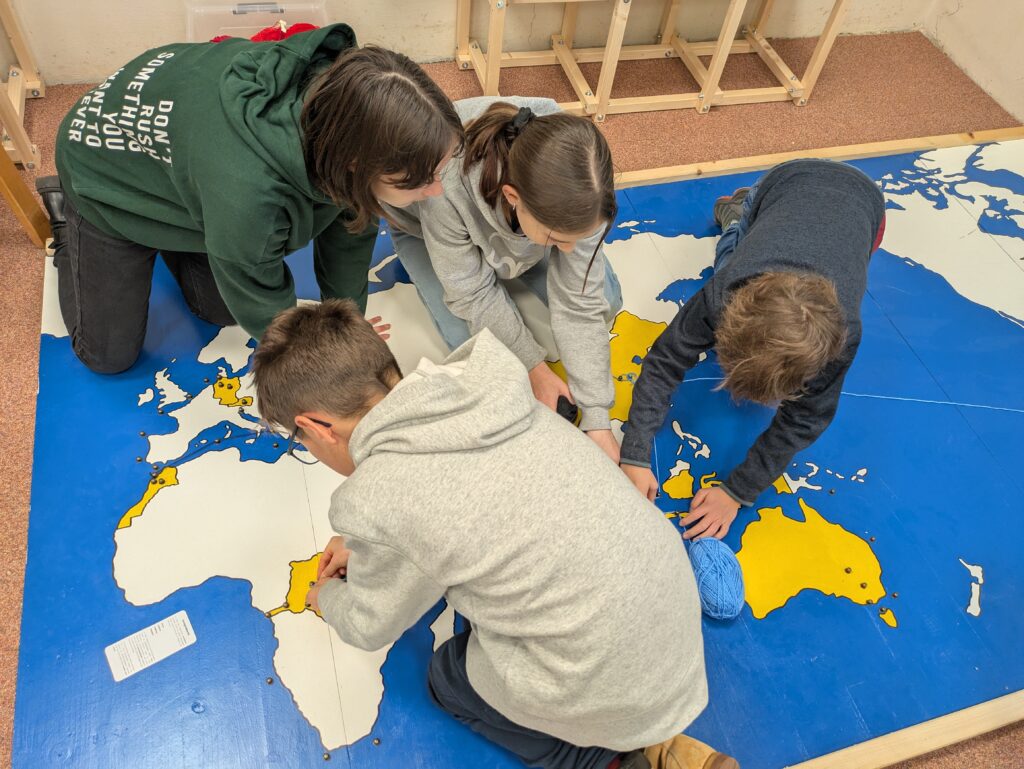 Kinder und Studentin legen den Weg der Produktion eines Smartphones auf einer großen Weltkarte