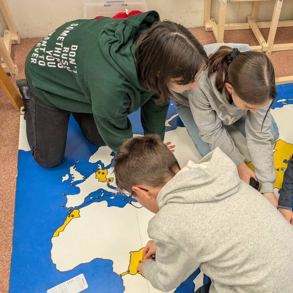 Kinder und Studentin legen den Weg der Produktion eines Smartphones auf einer großen Weltkarte