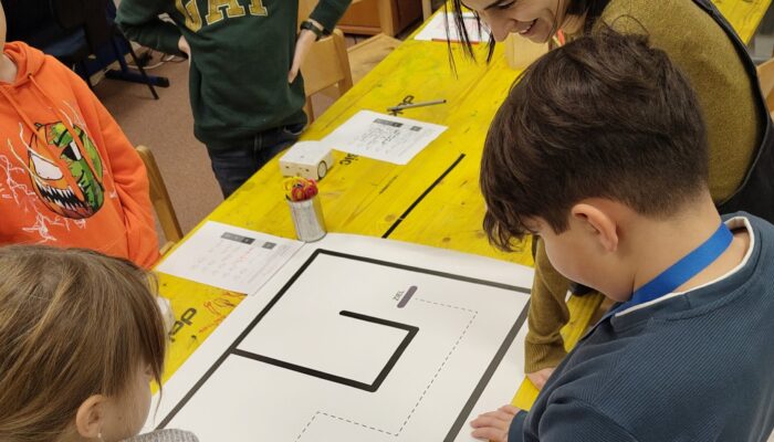 Kinder und TU Studierende, die einen Roboter einer Linie folgen lassen