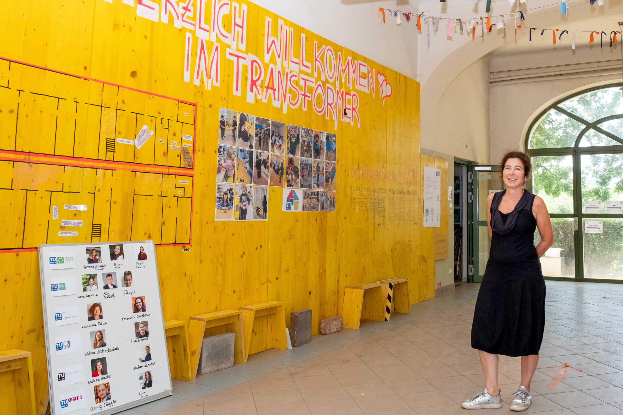 Eingangsbereich des TU Wien Transformer am Rennweg 89a mit dem Schriftzug „Herzlich Willkommen im Transformer“, Fotos von Kindern und Workshops, einem Raumplan zur Orientierung und Fahnen an der Decke