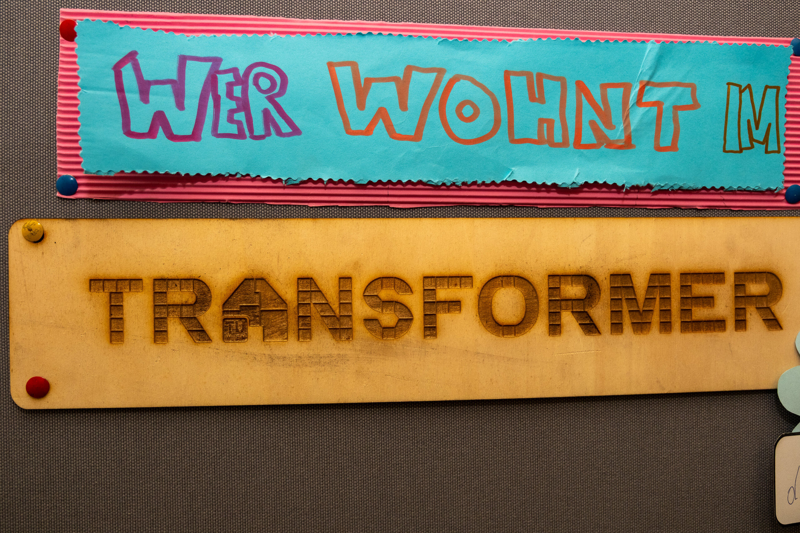 zwei Schilder mit Text "Wer wohnt im Transformer", erstellt aus Buntpapier und Holz graviert im Lasercutter